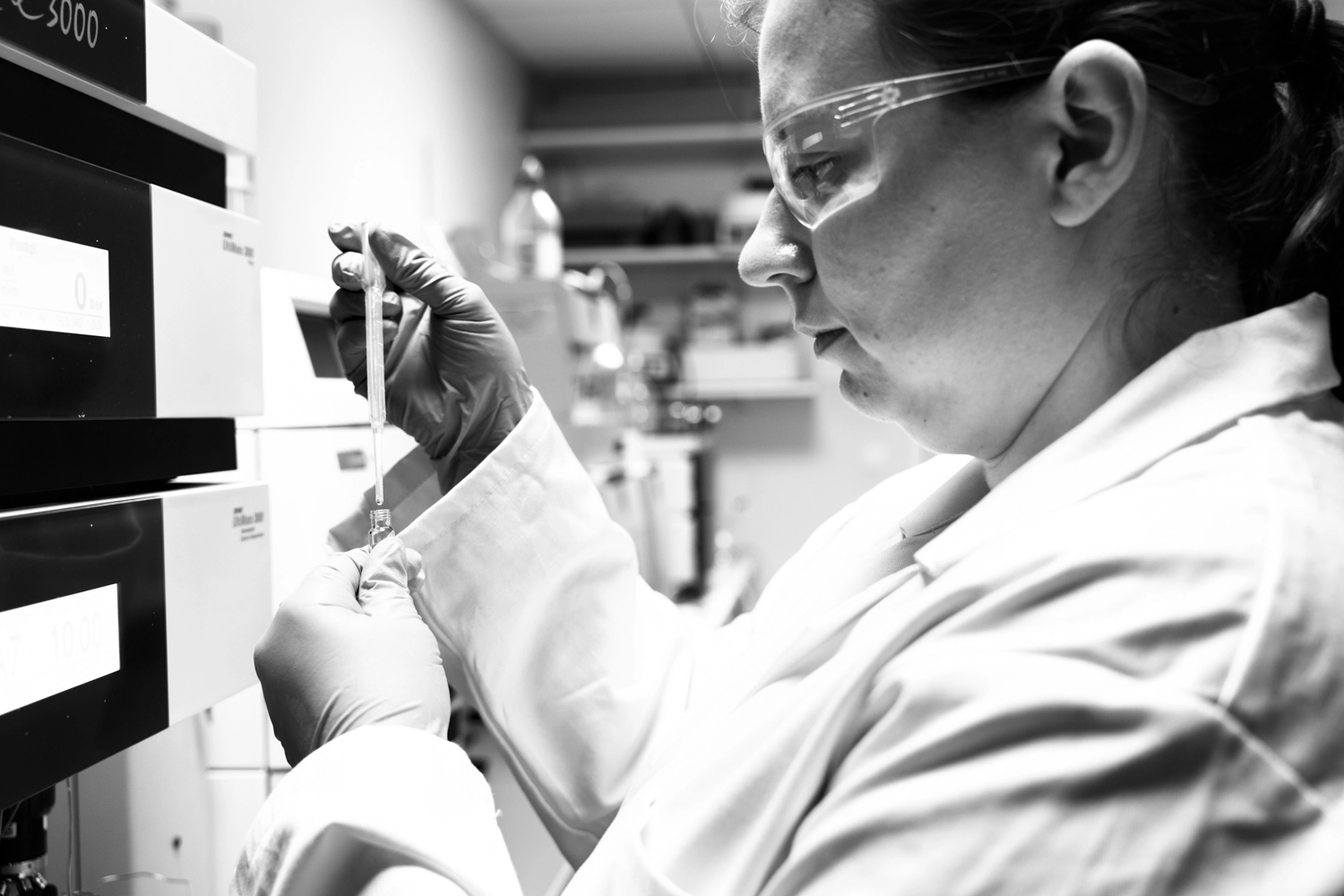 Portrait studio de la créatrice de parfums sur mesure Sarah Merciol, la fondatrice de Shesmou. La photographie est en noir et blanc et Sarah Merciol est en action. Dans son laboratoire, elle dose l'huile essentielle qu'elle va utiliser dans la création en cours. Photo ©Gaël Dupret - 2025